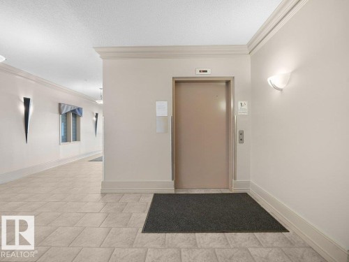 Elevator access, wall-mounted sconce lighting, crown molding, and tiled flooring - #116 16807 100 Av Nw, Edmonton, AB 