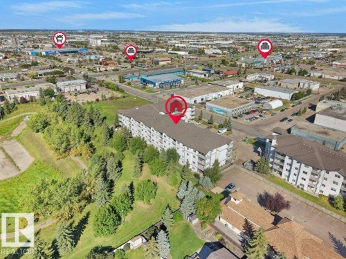 Multi-story building with multiple balconies, surrounded by mature trees and paved surfaces - #116 16807 100 Av Nw, Edmonton, AB 