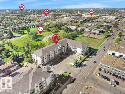 Aerial perspective of a multi-story residential building with a sloped roof, surrounded by green spaces and a paved road - #116 16807 100 Av Nw, Edmonton, AB 
