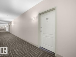 Hallway with patterned carpeting, white wall sconces, and a paneled entry door - 