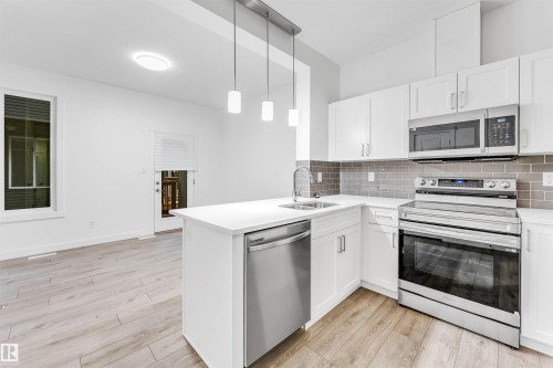 Kitchen featuring white cabinetry, stainless steel appliances, a white island, grey subway tile backsplash, and wood-finish flooring - #45 2710 66 St Sw, Edmonton, AB 