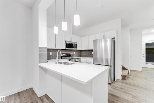 Kitchen featuring white cabinetry, stainless steel appliances, a subway tile backsplash, and light wood-finish flooring - #45 2710 66 St Sw, Edmonton, AB 