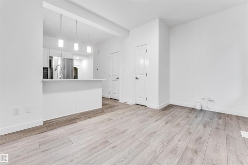 Wood-finish flooring throughout, stainless steel appliances, white kitchen cabinetry, kitchen island with seating, and pendant lighting - #45 2710 66 St Sw, Edmonton, AB 