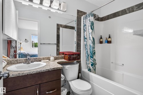 Bathroom featuring a built-in bathtub with integrated shelving, dark tile surround, a vanity with a light-toned countertop, and an undermount sink - 17363 120 Street Nw, Edmonton, AB 