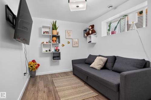 Wall-mounted television with visible wiring, wood-finish flooring, recessed window, and white walls - 17363 120 Street Nw, Edmonton, AB 