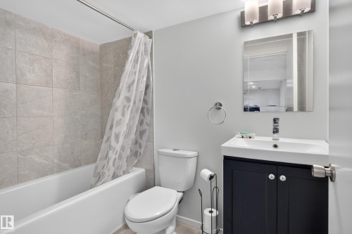 Bathroom featuring a white tub, light-toned tile shower surround, dark wood-finish vanity with white countertop, and a vanity mirror with sconce lighting - 17363 120 Street Nw, Edmonton, AB 