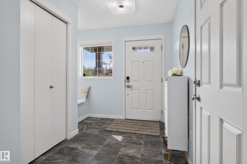 Entryway featuring dark tile flooring, a built-in window bench, a white paneled entry door with transom lites, and bi-fold closet doors - 17363 120 Street Nw, Edmonton, AB 