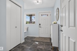 Entryway featuring dark tile flooring, a built-in window bench, a white paneled entry door with transom lites, and bi-fold closet doors - 