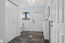 Entryway featuring dark tile flooring, a built-in window bench, a white paneled entry door with transom lites, and bi-fold closet doors - 17363 120 Street Nw, Edmonton, AB 