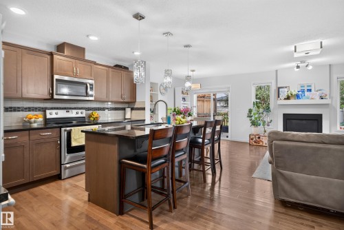 Kitchen featuring stainless steel appliances, dark countertops, wood-finish flooring, and an island with pendant lighting - 17363 120 Street Nw, Edmonton, AB 