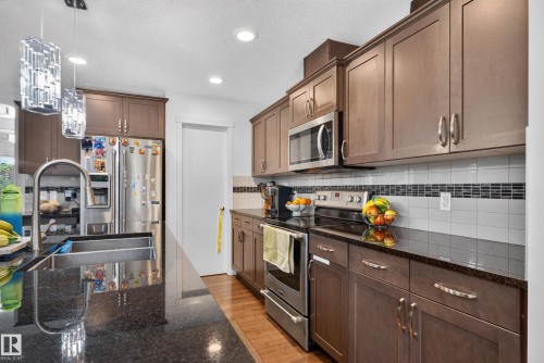 Kitchen featuring wood-finish cabinetry, stainless steel appliances, dark stone countertops, tile backsplash with decorative accent, and recessed lighting - 17363 120 Street Nw, Edmonton, AB 