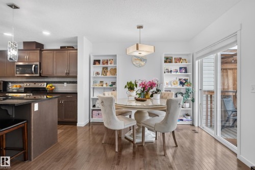 Wood-finish flooring throughout, kitchen with dark cabinetry and stainless steel appliances, built-in shelving, dining area with a modern chandelier, and a sliding glass door - 17363 120 Street Nw, Edmonton, AB 