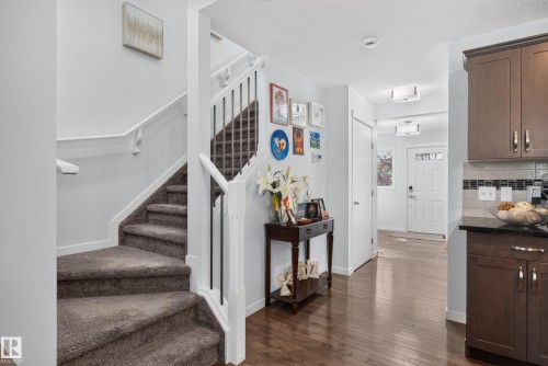 Carpeted staircase with white risers and railings, wood-finish flooring, white paneled interior doors, dark wood-finish cabinetry, and black countertop - 17363 120 Street Nw, Edmonton, AB 