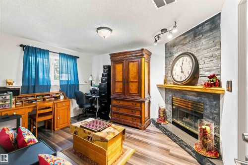 Wood-finish flooring throughout, stone-clad fireplace with mantel, built-in lighting, and a window providing natural light - #6 15 Poirier Av, St. Albert, AB 