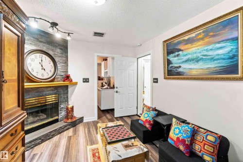 Stacked stone fireplace with a gold-finish mantel, track lighting, and wood-finish flooring - #6 15 Poirier Av, St. Albert, AB 