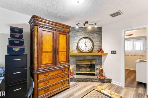 Stacked stone fireplace with a wood mantle, recessed fireplace insert, and track lighting - #6 15 Poirier Av, St. Albert, AB 