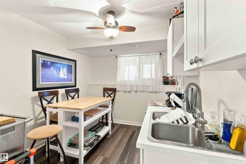 Efficient kitchen layout featuring stainless steel sink with faucet, white cabinetry with upper storage, wood-finish flooring, and adjacent dining area with seating for four - #6 15 Poirier Av, St. Albert, AB 