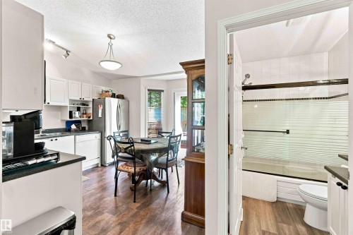 Kitchen with wood-finish flooring, white cabinetry, stainless steel refrigerator, and integrated dining space - #6 15 Poirier Av, St. Albert, AB 