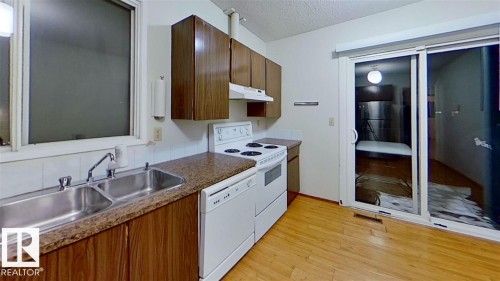 Kitchen featuring wood-finish cabinetry, a double basin stainless steel sink, granite-style countertops, white tile backsplash, and wood-finish flooring - 4611 52 Avenue, Stony Plain, AB 