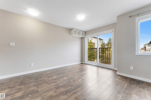 Wood-finish flooring, light neutral wall color, white ceiling, two ceiling-mounted light fixtures, sliding glass door to exterior, white trim - 3340 15A Avenue Nw, Edmonton, AB 
