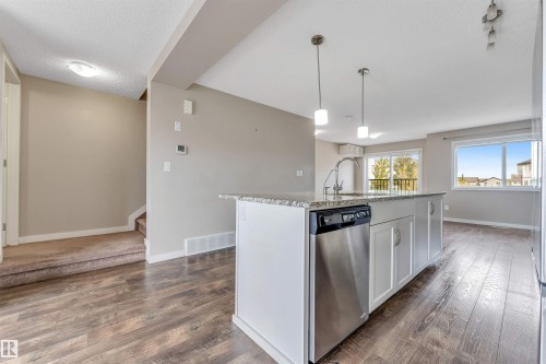 Kitchen island featuring a stainless steel dishwasher, white cabinetry, and a granite-style countertop - 3340 15A Avenue Nw, Edmonton, AB 