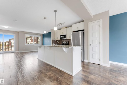 Open-concept living space with wood-finish flooring, white cabinetry, a kitchen island, and stainless steel appliances - 3340 15A Avenue Nw, Edmonton, AB 