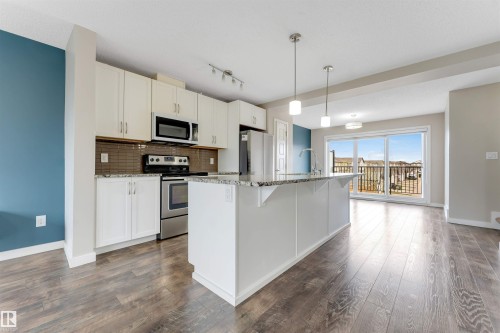 Kitchen featuring white cabinetry, stainless steel appliances, granite countertops, and a full-height tile backsplash - 3340 15A Avenue Nw, Edmonton, AB 