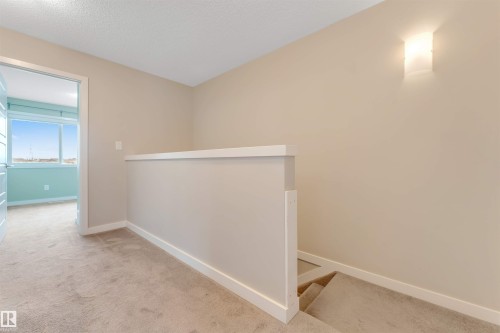 Carpeted hallway with a neutral color palette, integrated wall sconce, and a partial balustrade overlooking a carpeted staircase - 3340 15A Avenue Nw, Edmonton, AB 