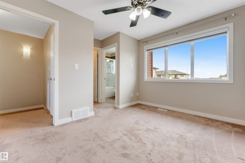 Expansive room featuring neutral-toned carpet, a large window, and a ceiling fan with integrated lighting - 3340 15A Avenue Nw, Edmonton, AB 
