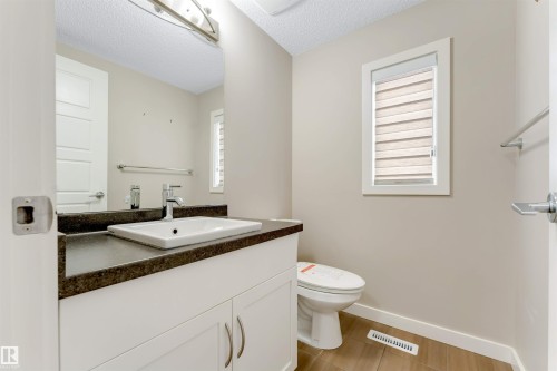 White vanity with dark countertop, integrated rectangular sink, wall-mounted mirror, and wood-finish flooring - 3340 15A Avenue Nw, Edmonton, AB 
