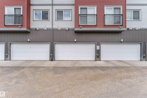 Attached garage doors, corrugated metal siding, red and gray exterior paneling, and upper-level balconies with black railings - 3340 15A Avenue Nw, Edmonton, AB 