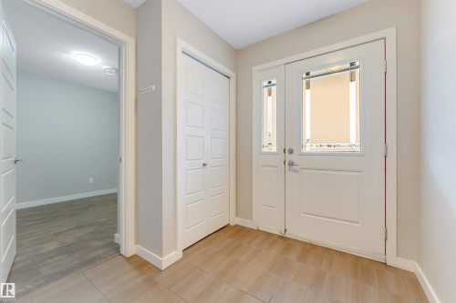 Entryway featuring light-toned tile flooring, a double front door with integrated window panels, and a bi-fold closet with panel detailing - 3340 15A Avenue Nw, Edmonton, AB 