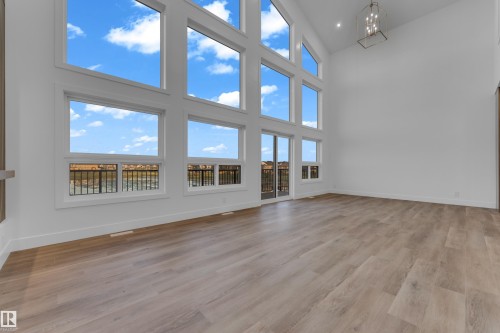 Two-story living area with high ceilings, expansive windows, wood-finish flooring, and a modern chandelier - 236 Linden Loop, Leduc, AB 