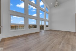 Two-story living area with high ceilings, expansive windows, wood-finish flooring, and a modern chandelier - 