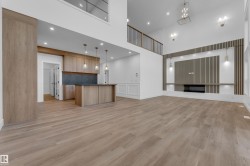 Open-concept living space featuring wood-finish flooring, a contemporary fireplace with a slatted accent wall, and a kitchen island with pendant lighting - 