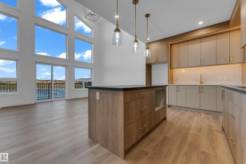 Soaring vaulted ceilings with expansive windows, contemporary kitchen island with dark countertop, elegant gold-tone hardware, wood-finish flooring, and modern pendant lighting - 236 Linden Loop, Leduc, AB 