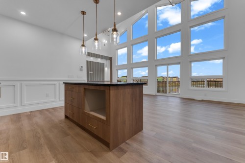 Vaulted ceilings with expansive window arrays, wood-finish flooring, a kitchen island with dark countertop, and decorative wall paneling - 236 Linden Loop, Leduc, AB 