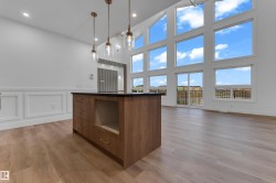 Vaulted ceilings with expansive window arrays, wood-finish flooring, a kitchen island with dark countertop, and decorative wall paneling - 
