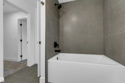 White bathtub with dark gray shower tile, matte black shower fixtures, and gray floor tile - 