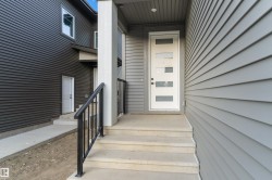 Modern exterior entrance with a white door featuring frosted glass panels, concrete steps, black metal handrails, and horizontal siding - 