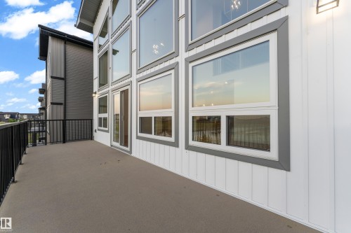 Modern exterior featuring expansive multi-pane windows with aluminum framing, horizontal corrugated metal siding accents, and a spacious concrete deck with metal railings overlooking the surrounding landscape - 236 Linden Loop, Leduc, AB 