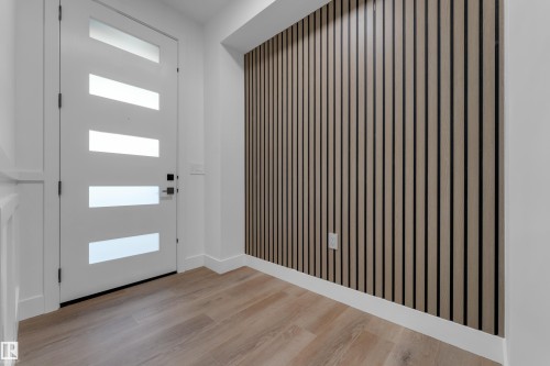 Modern white entry door with frosted glass inserts, wood-finish flooring, and a textured accent wall - 236 Linden Loop, Leduc, AB 