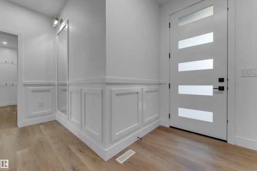 Entryway featuring wood-finish flooring, wainscoting, a full-length mirror, and a modern door with horizontal opaque glass panels - 236 Linden Loop, Leduc, AB 