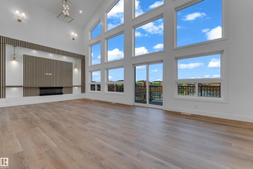 Vaulted ceiling with a contemporary chandelier, wood-finish flooring, built-in fireplace, and expansive windows - 236 Linden Loop, Leduc, AB 