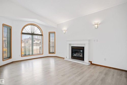 Bright room featuring wood-finish flooring, a classic fireplace with a white mantel, and an arched window with wood trim - 2915 151A Avenue Nw, Edmonton, AB 