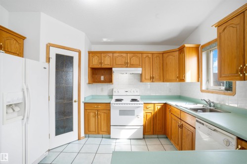 Kitchen featuring white appliances, light wood-finish cabinetry, light blue countertops, and white square tile flooring - 2915 151A Avenue Nw, Edmonton, AB 