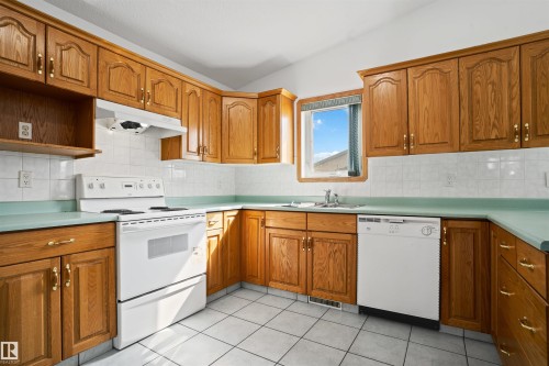 Kitchen featuring wood cabinetry, white tile flooring, and white appliances - 2915 151A Avenue Nw, Edmonton, AB 