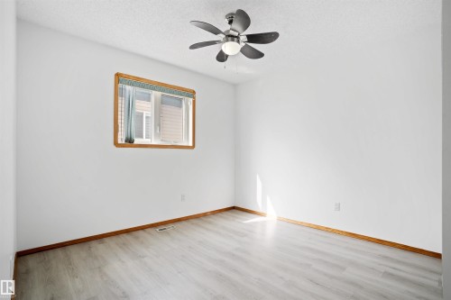 Room with a ceiling fan, a window with wood trim, wood-finish flooring, and white walls - 2915 151A Avenue Nw, Edmonton, AB 
