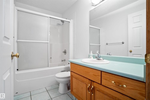 White bathtub with sliding glass doors, a single vanity with wood-finish cabinetry, a white basin sink, and a large wall-mounted mirror - 2915 151A Avenue Nw, Edmonton, AB 