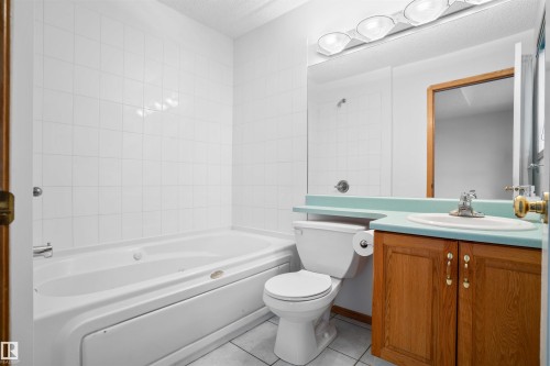 White tiled bath surround, soaking tub, wood-finish vanity, integrated sink, and wall-mounted mirror - 2915 151A Avenue Nw, Edmonton, AB 